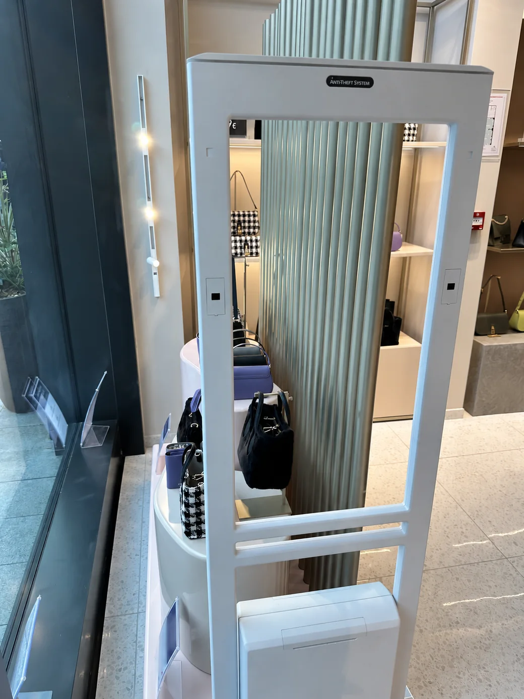 Portique antivol blanc à côté de présentoirs de sacs.