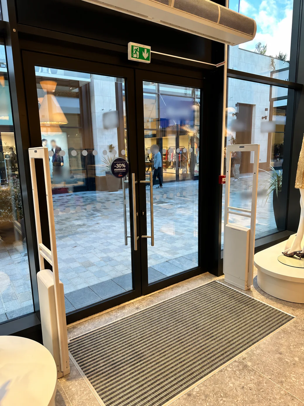 Deux portiques antivol blancs encadrant la porte vitrée d’une boutique.